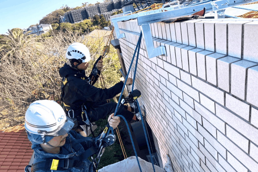 ロープで外壁タイルの調査を行う作業員